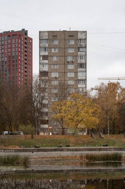 1970 'lerin prefabrik apartmanı. Yüzü yıpranmış. Etrafı güz ağaçları ve göletlerle çevrili. Arka planda modern bir gökdelen görülebilir. Vynohradar, Kyiv, Ukrayna - Kasım 2024.