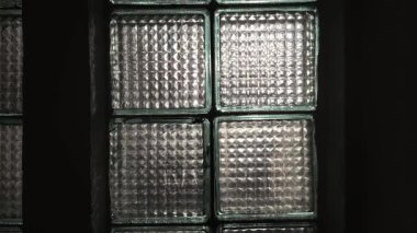 Pencere çerçevesindeki cam bloklar, içinden doğal ışık yansıyor. Kare desenli cam fayanslar geometrik yarı saydam bir yüzey oluşturur