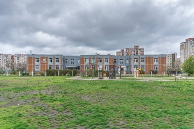 Turuncu ve gri fayanslı modern iki katlı anaokulu binası. Ön planda çocuk parkı görünüyor. Troieshchyna İlçesi, Kyiv, Ukrayna 6 Nisan 2025.