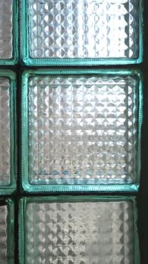 Pencere çerçevesindeki cam bloklar, içinden doğal ışık yansıyor, dolly dışarı. Kare desenli cam fayanslar geometrik yarı saydam bir yüzey oluşturur