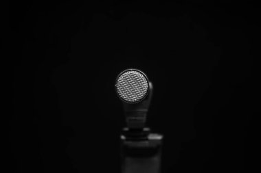 Siyah zemin üzerinde metal ağ bulunan yuvarlak gümüş bir mikrofon..