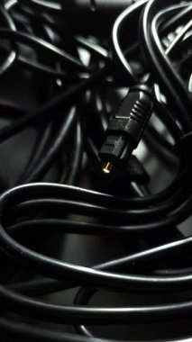 Altın kaplama uçlu optik ses kablosu siyah kablolar arasında yanıp sönüyor..