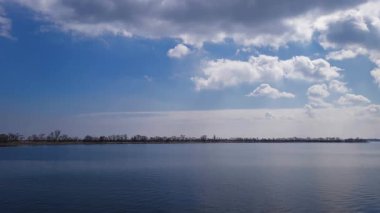 Sakin bir nehir ve bulutlu gökyüzünün altındaki uzak ağaçlar aydınlık bir günde.