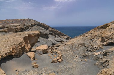 Tenerife 'nin güneyinde volkanik kayalar ve kum oluşumları, okyanus, ufuk ve gökyüzü bulutlu arka plan, Granadilla de Abona, Kanarya adaları