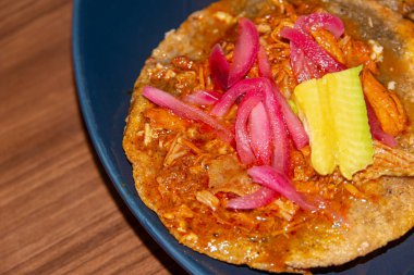 Panucho 'nun otantik lezzetlerini deneyin. Kızarmış fasulyeyle doldurulmuş ve üzerinde kochinita pibil, turşulu soğan ve baharatlı habanero sosu bulunan geleneksel bir Meksika yemeği.