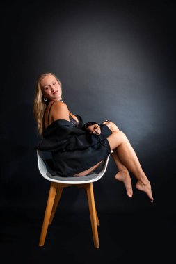 Kendine güvenen sarışın bir kadın zarif poz verir, narin iç çamaşırlarının üzerine siyah bir ceket giyer.