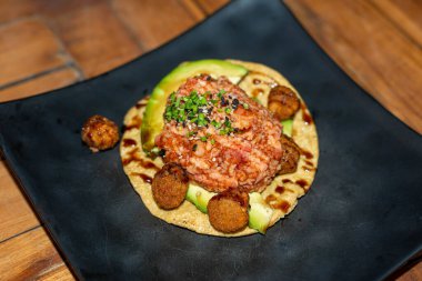 Close-up of a gourmet tuna tostada topped with avocado and spices, served with croquettes. A delicious and colorful dish that combines fresh seafood with authentic Mexican flavors.