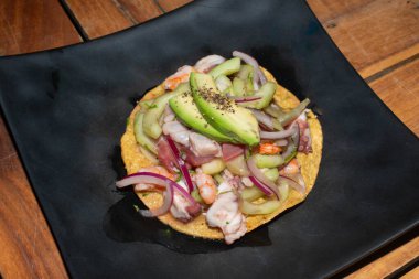 Close-up of a traditional Mexican tostada topped with shrimp, tuna, octopus ceviche, cucumber, avocado, and red onion. A fresh and colorful seafood dish full of authentic flavors.