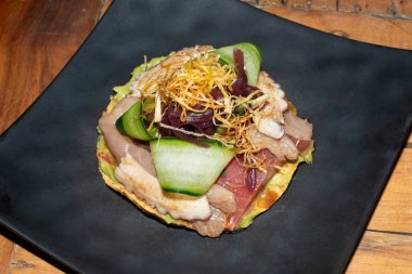 Close-up of a Mexican tostada topped with fish, squid, tuna ceviche, cucumber, guacamole, and wheat sprouts. A fresh and colorful seafood dish with authentic Mexican flavors.