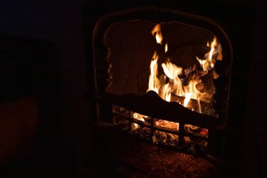 Karanlık odada ateş saçan sarı diller. Alev dilleri. Siyah arka plan. Şöminede yangın var. Çatırdayan kütükler. Ev rahatlığı. Kışın ısınma.