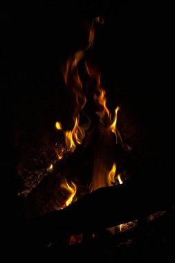Karanlık odada ateş saçan sarı diller. Alev dilleri. Siyah arka plan. Şöminede yangın var. Çatırdayan kütükler. Ev rahatlığı. Kışın ısınma.