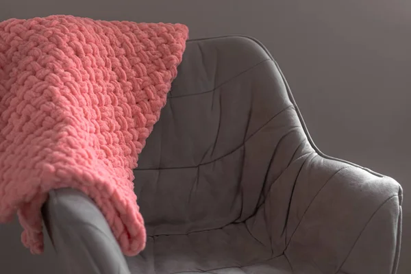 A plush blanket on a chair in a home interior. Plush blanket. A knitted blanket on the chair. Home interior. Home comfort. Homemade blanket. Plush yarn. Warm in winter. Knitted items in the interior.