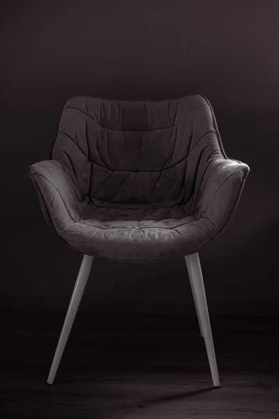Dining chair. A soft chair. Silhouette of a chair. Comfortable home furniture. A chair with a back and armrests. Black and white photo. Upholstered furniture in subdued light