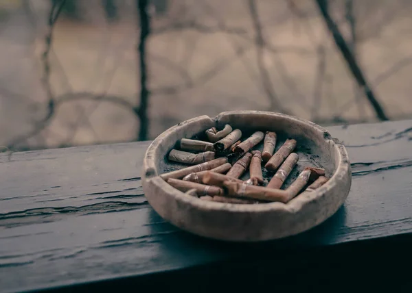 木製のテラスビームにバットを持つ粘土灰皿 路上でタバコを吸う タバコの残骸だ ニコチン中毒 タバコの吸い殻で灰皿 危険な癖だな — ストック写真