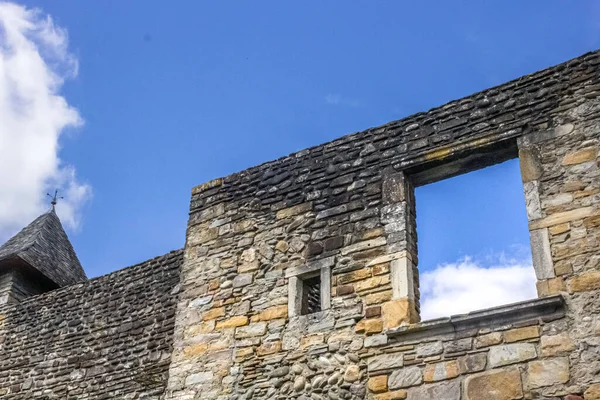 A stone wall of an ancient building with a view to the sky through a window without glass. Photographed through the window. Window without glass. Stone wall. Old house. View of the sky. Window hole. Camino de Santiago. The Way of St. James.