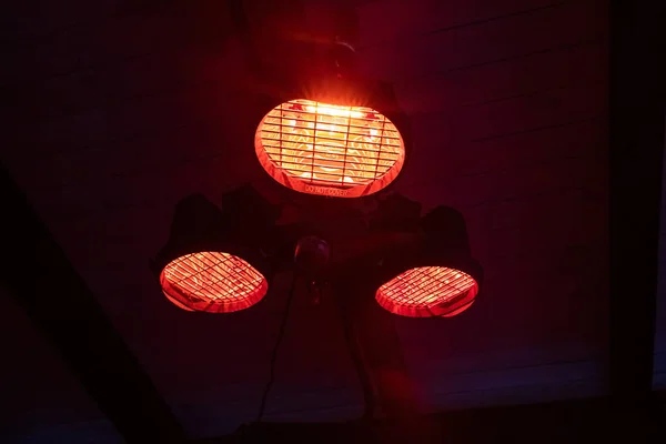 Street heater. Heat source. Equipment on the home terrace. Red light. Summer playground in the cafe. Street heater with three lamps.