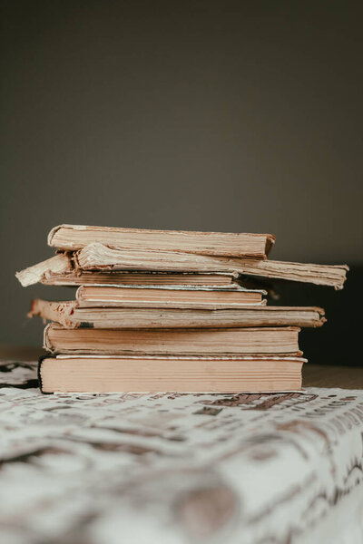 A stack of old books with frayed spines and yellowed pages. Book pages are yellow from old age. Many books. Source of knowledge. Old library. Vintage background. Yellow pages. An open book. Worn book spines.