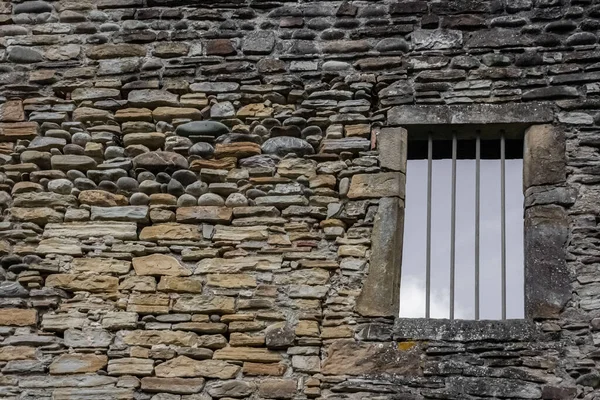 A window opening with an iron grate in a stone wall. A window opening with an iron grate in a stone wall. Stone wall. Ancient architecture. Old Europe. Stone background. French village.