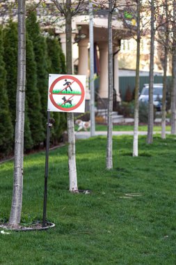 Üzerinde yazı olan bir tabela çimlerde köpekleri gezdirmez. Köpek gezdirmek yasaktır. Bilgi plakası. Uyarı işareti. Davranış Kuralları. Avlunun temizliği. Köpek sahipleri için uyarı. Kesilmiş çimenler.