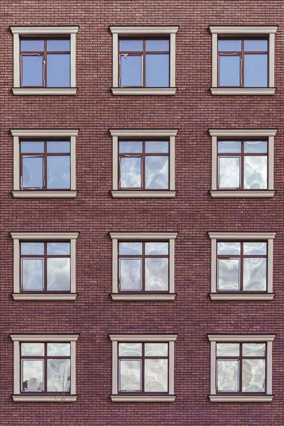 The facade of a brick house with identical square windows. Facade of the house. Brick wall. Many floors. Glazed windows. Geometry in architecture. Outer wall.