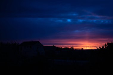 Gün batımı gökyüzü. Evlerin ve ağaçların silueti. Akşam bulutlarının renkleri. Ukrayna doğası. Sessiz bir akşam. Huzurlu bir gökyüzü. Gün batımında mavi-kırmızı gökyüzü Köyün siluetinin üstünde.