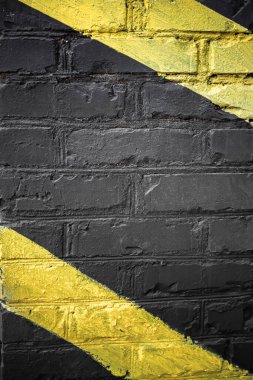 Üzerinde çapraz sarı çizgiler olan siyah tuğla bir duvar. Siyah üstüne sarı. Tuğla. Tuğla bir duvarda siyah boya. Sert bir yüzey. Garajı tasarlıyorum. İçerde tuğla var..