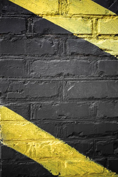 Black brick wall with diagonal yellow lines on it. Yellow on black. Brick background. Black paint on a brick wall. Rough surface. Designing the garage. Brick in the interior.