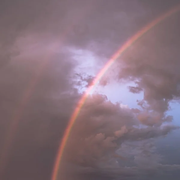 Double rainbow on the background of the cloudy sky. A bright rainbow. A multi-colored phenomenon of nature. Heavenly landscape. Cloudy sky. Rainy weather. After the storm.