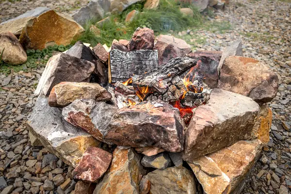 Fireplace among the stones with a view of the mountains and the lake. Mountain tourism. A trip to the Ukrainian Carpathians. Tongues of flame. Stones for barbecue. Warming up by the fire. Romance of the mountains. Fall nature.