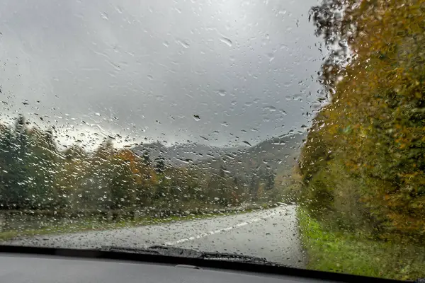 stock image Raindrops on the glass. Bright autumn road. Raindrops on the windshield of the car. Gloomy autumn weather. Rainy season. Road trip. Fall colors.