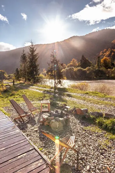 Wooden deck chairs. Rest in the mountains. Mountain and river view. The seats are outside. Wooden furniture. Autumn vacation. Autumn landscape in the sunset rays.