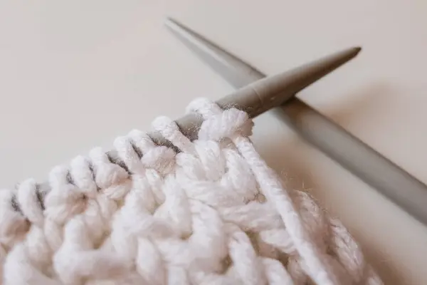 Knitting with knitting needles. Loops on a knitting needle. A quiet hobby. White voluminous yarn. Wool thread. Knitted warm things. English rubber band. Knitting scheme. Female hands.