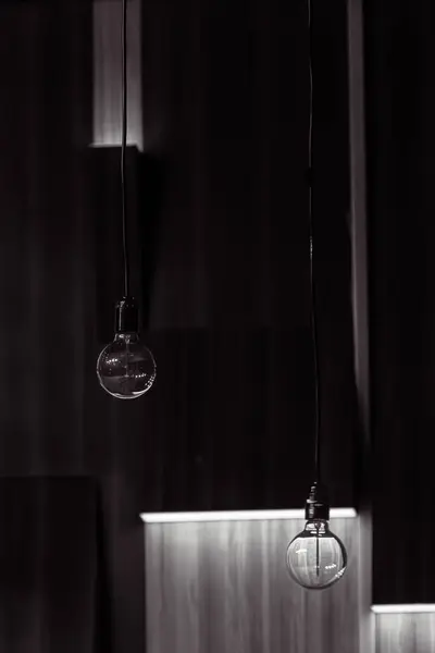 Electric light source. Light symbol. Achievements of humanity. Evidence of progress. Hanging from the ceiling by a wire. A round transparent electric light bulb on a dark background.