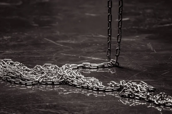 Iron chain on a dark background. Chain links. Solid rope. Steel structure. Sequential connection of rings. Long cargo chain. Accessory for sadomasochism. Black and white.