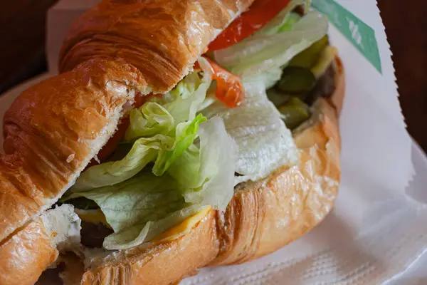 A fresh croissant with a juicy filling of vegetables, cheese, salad and meat. Crispy croissant crust. Sandwich with vegetables and meat. European nutritious snack. Tasty fast food. Sandwich in male hands. Pastry with filling.