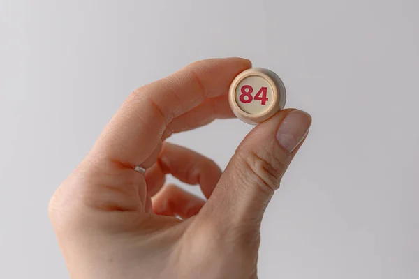 Lotto barrel with the number 84 in a woman\'s hand. Female hand. Lotto keg. A two-digit number. Woman 40 years old. Symbol of the 40th anniversary. Year of birth 1984. Hold in hand. Age metaphor.