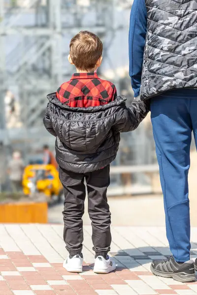 Bir çocuk babasının elini tutar. Küçük bir çocuğun arka görüntüsü. Bilinmeyen gelecek. Ebeveyn desteği. Bekar bir baba. Yetim bir çocuk. Bir yetişkin ve bir çocuk. Ukrayna 'da çocukluk. Çocukların korunması.