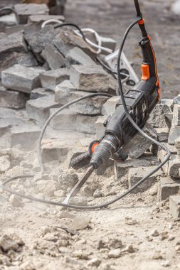 Kaldırımdaki kaldırım taşlarını tamir etmek için endüstriyel bir araç. Bir adam eski kaldırım taşlarını delgiyle kaldırır. İnşaat alanında matkap, kürek, kazma ve çekiç. Yol tamiri. Ev aletleri. Bir adam kaldırım taşlarının altındaki kumu bir malayla düzleştiriyor..