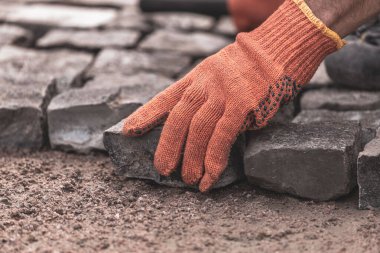 Koruyucu eldivenli adamların elleri kaldırım taşları döşüyorlar. Yolların ve kaldırımların tamiri. Döşeme taşları koyun. Hayat restorasyonu. Çalışkan bir adam. Taş yol.