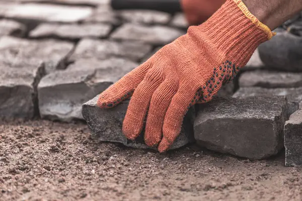 Koruyucu eldivenli adamların elleri kaldırım taşları döşüyorlar. Yolların ve kaldırımların tamiri. Döşeme taşları koyun. Hayat restorasyonu. Çalışkan bir adam. Taş yol.
