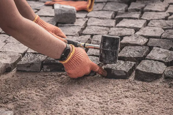Koruyucu eldivenli adamların elleri kaldırım taşları döşüyorlar. Yolların ve kaldırımların tamiri. Döşeme taşları koyun. Hayat restorasyonu. Çalışkan bir adam. Taş yol.