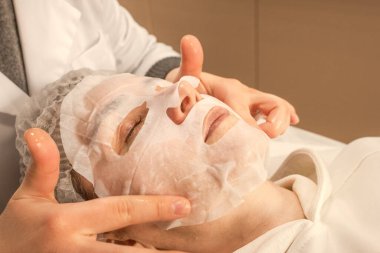 Kumaş kozmetik maske. Güzelliğin, gençliğin ve ışıl ışıl tenin sırrı. Yaşlanma önleyici cilt bakımı 40 +. Kozmetik prosedürü. Deri hidrasyonu. Yüz bakımı. Kadın güzelliği. Güzellik tedavisi. Güzellik salonu. Güzellik ayini. Yüzünde maskeyle yatan bir kadın..