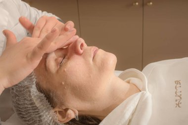 Profesyonel güzellik uzmanı. Bir kozmetolojistin müşterisi. Kendi başının çaresine bakma alışkanlığı. Bakım prosedürleri. Güzellik ve gençlik sırları. Kadın suratı. Kırışıkların ve yaşlanmanın önlenmesi. Güzellik salonu. Kozmetik ameliyatları sırasında genç bir kadın kanepede yatıyor..