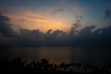 Hint Okyanusu 'nun üzerinde muhteşem bir gün doğumu, sakin sular sabah güneşlerini yansıtıyor ve kıyı tropikal palmiyeleri bu güzel manzarayı tamamlıyor.