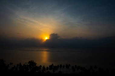 Hint Okyanusu 'nun üzerinde muhteşem bir gün doğumu, sakin sular sabah güneşlerini yansıtıyor ve kıyı tropikal palmiyeleri bu güzel manzarayı tamamlıyor.