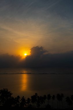 Hint Okyanusu 'nun üzerinde muhteşem bir gün doğumu, sakin sular sabah güneşlerini yansıtıyor ve kıyı tropikal palmiyeleri bu güzel manzarayı tamamlıyor.