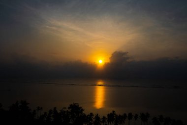 Hint Okyanusu 'nun üzerinde muhteşem bir gün doğumu, sakin sular sabah güneşlerini yansıtıyor ve kıyı tropikal palmiyeleri bu güzel manzarayı tamamlıyor.