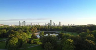 Arka planda şehir merkezi olan şehir parkı. Varşova panoramasının üzerindeki gökdelenlerdeki ofislerin şehir parkındaki havadan görüntüsü. Yaz boyunca yeşil ağaçlarla dolu parkta göl.