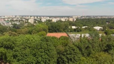 Tenis merkezi, turuncu kortlar, ağaçlar ve yukarıdan park. Hava Görünümü