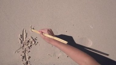 Genç bir kız kumsaldaki beyaz kumlara tatil kelimesi yazıyor..